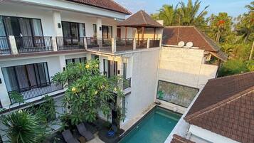 A two-story building with a swimming pool, outdoor seating, and a garden area.
