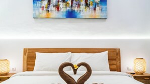 A hotel room with a wooden headboard, white bedding, a heart-shaped towel arrangement, and a painting on the wall. - Balian Paradise Hotel (Selemadeg)