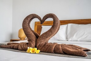 A neatly made heart shape with towels on a bed, accompanied by a yellow flower. - Balian Paradise Hotel (Selemadeg)