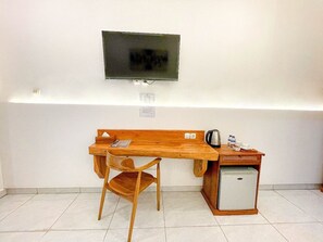 A small room with a wooden desk, a chair, a television mounted on the wall, and a small refrigerator.