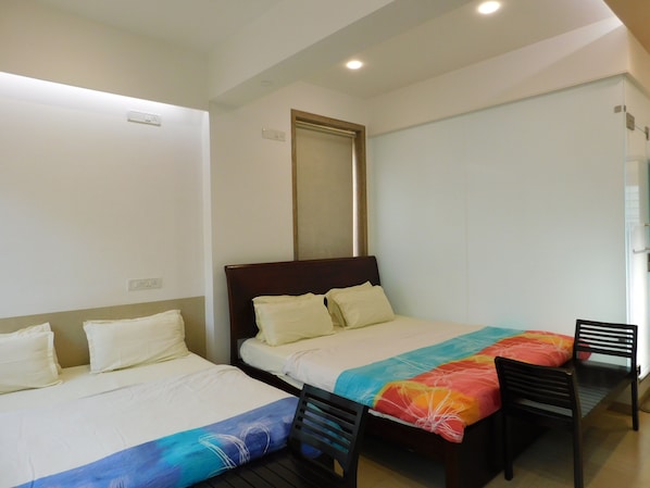 A hotel room with two single beds, a wooden headboard, a colorful bedspread, a small table with two chairs, and a mirror on the wall.