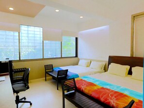 A hotel room with a bed, two chairs, a desk, and large windows.