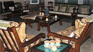A traditional living room with vintage furniture, including a sofa set and armchairs, a coffee table, and a television. - Tshimologo Farm Guest House (Francistown)