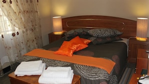 A neatly made bed with a dark headboard, two bedside lamps, and a wooden nightstand with a lamp. - Tshimologo Farm Guest House (Francistown)