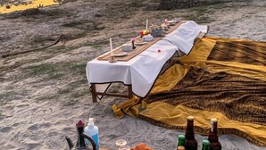 A beach picnic setup with a table, blankets, and bottles.