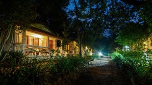 A pathway leading to a building with a thatched roof, surrounded by lush greenery.