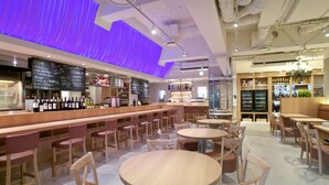A modern bar area with a long counter, multiple stools, and round tables. There are shelves with bottles and a chalkboard menu. - Fukuoka Toei Hotel (Fukuoka)