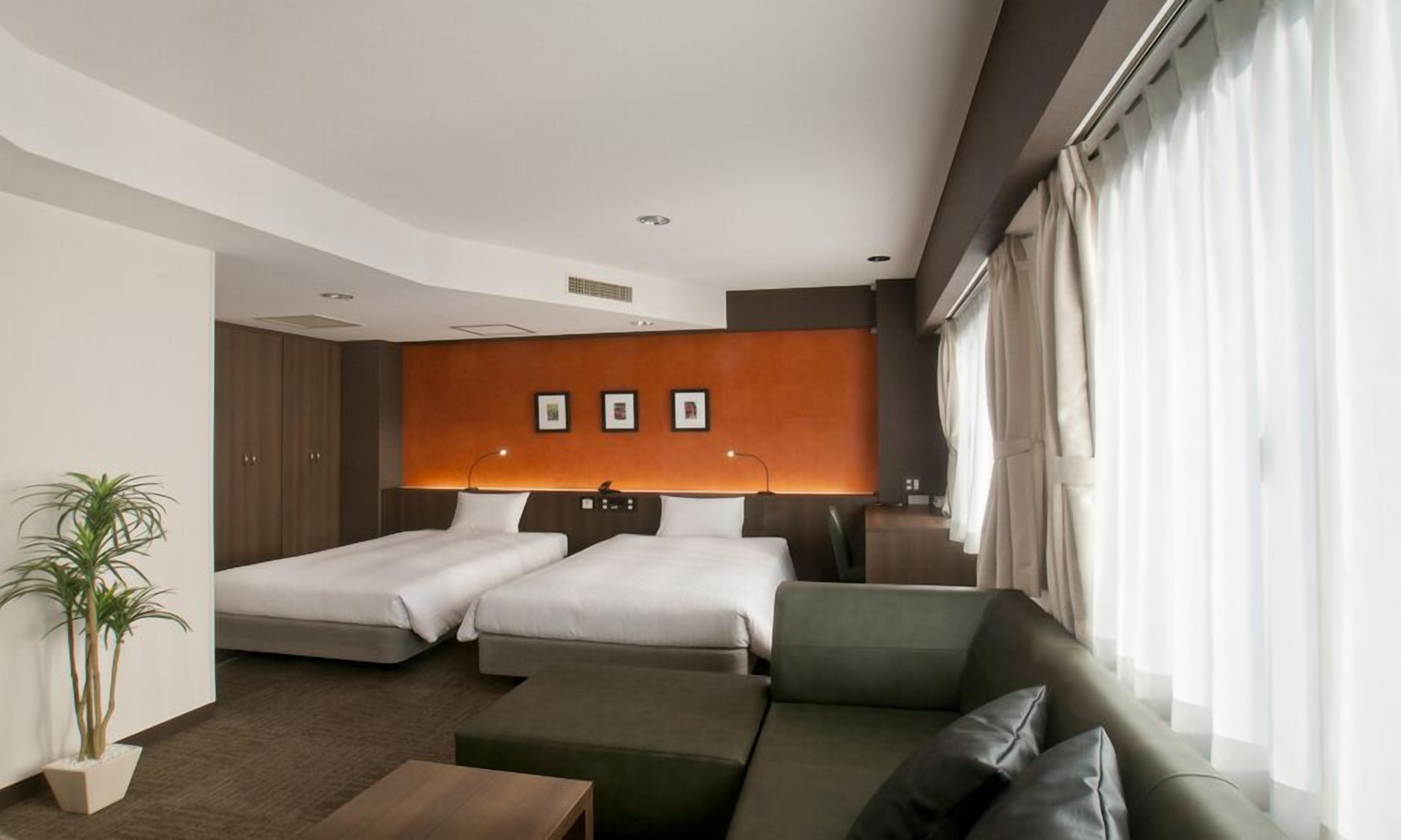 Habitación de hotel con dos camas, un sofá, una mesita, una planta en maceta y una pared con tres cuadros enmarcados.