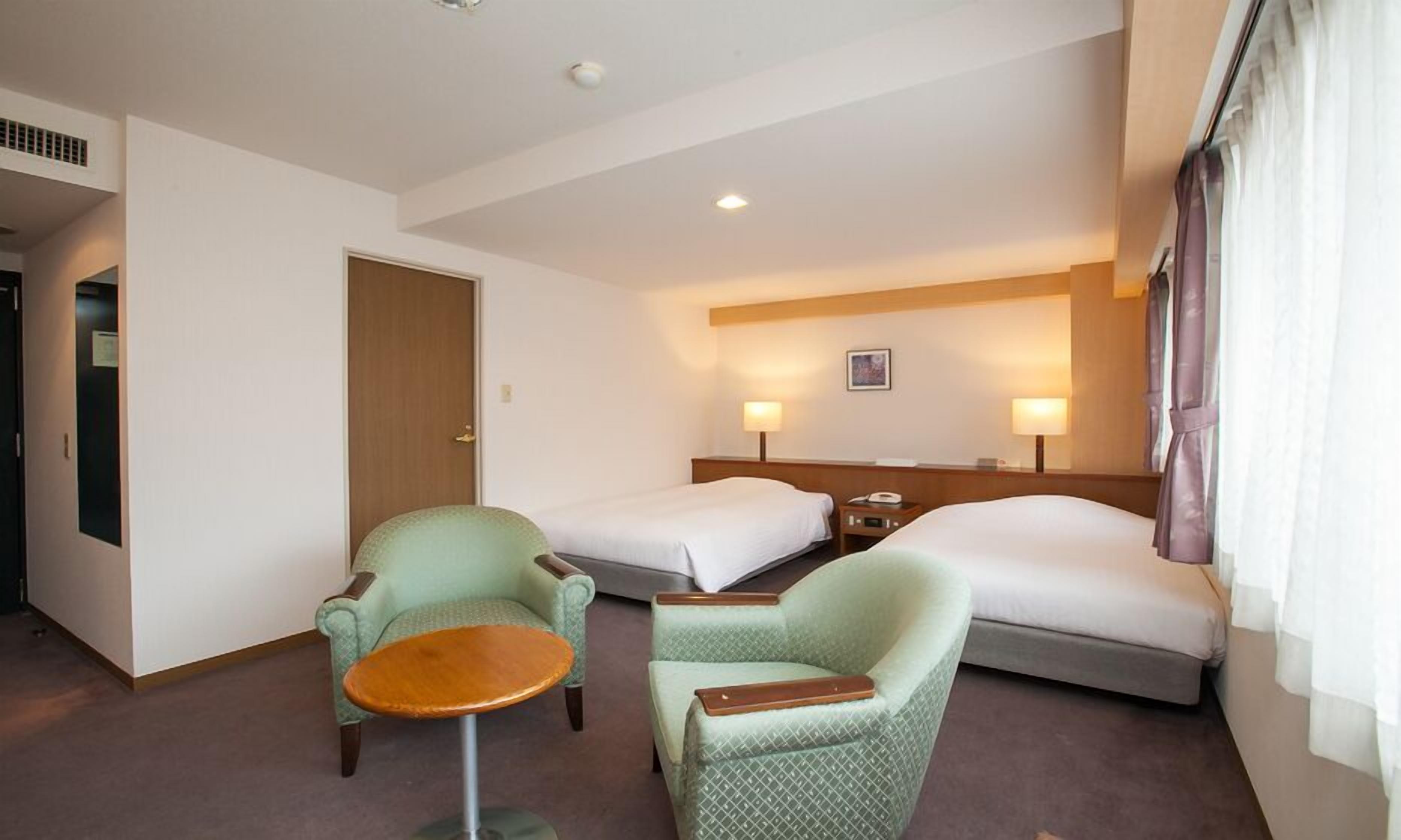 Una habitación de hotel con dos camas individuales, un escritorio pequeño, dos sillones y una mesita.