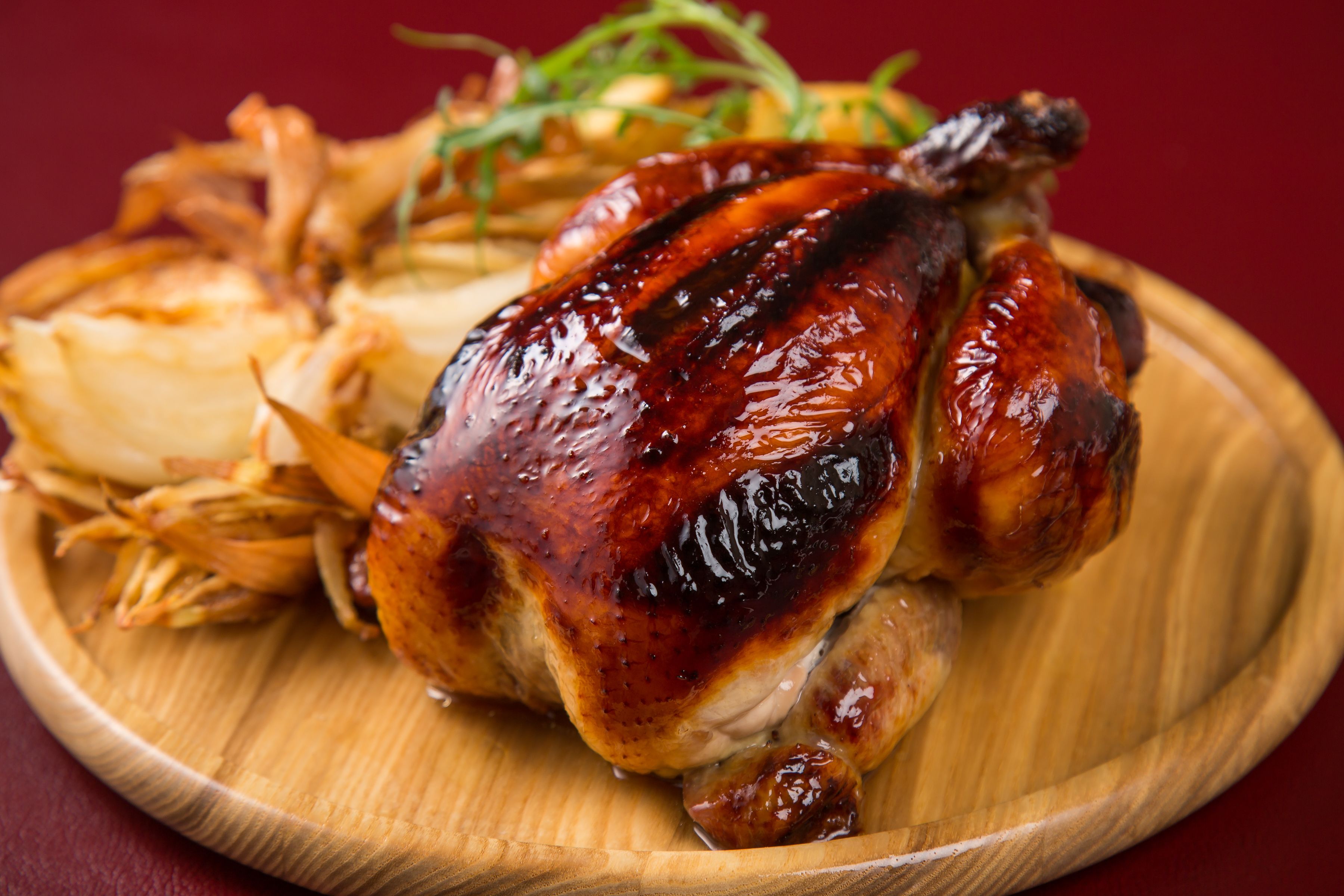 Un pollo asado sobre un plato de madera con algunas verduras.