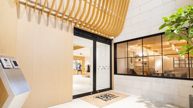 A hotel entrance with a modern design, including a wooden slatted wall, a glass door, and a reception area visible through the window. - Fukuoka Toei Hotel (Fukuoka)