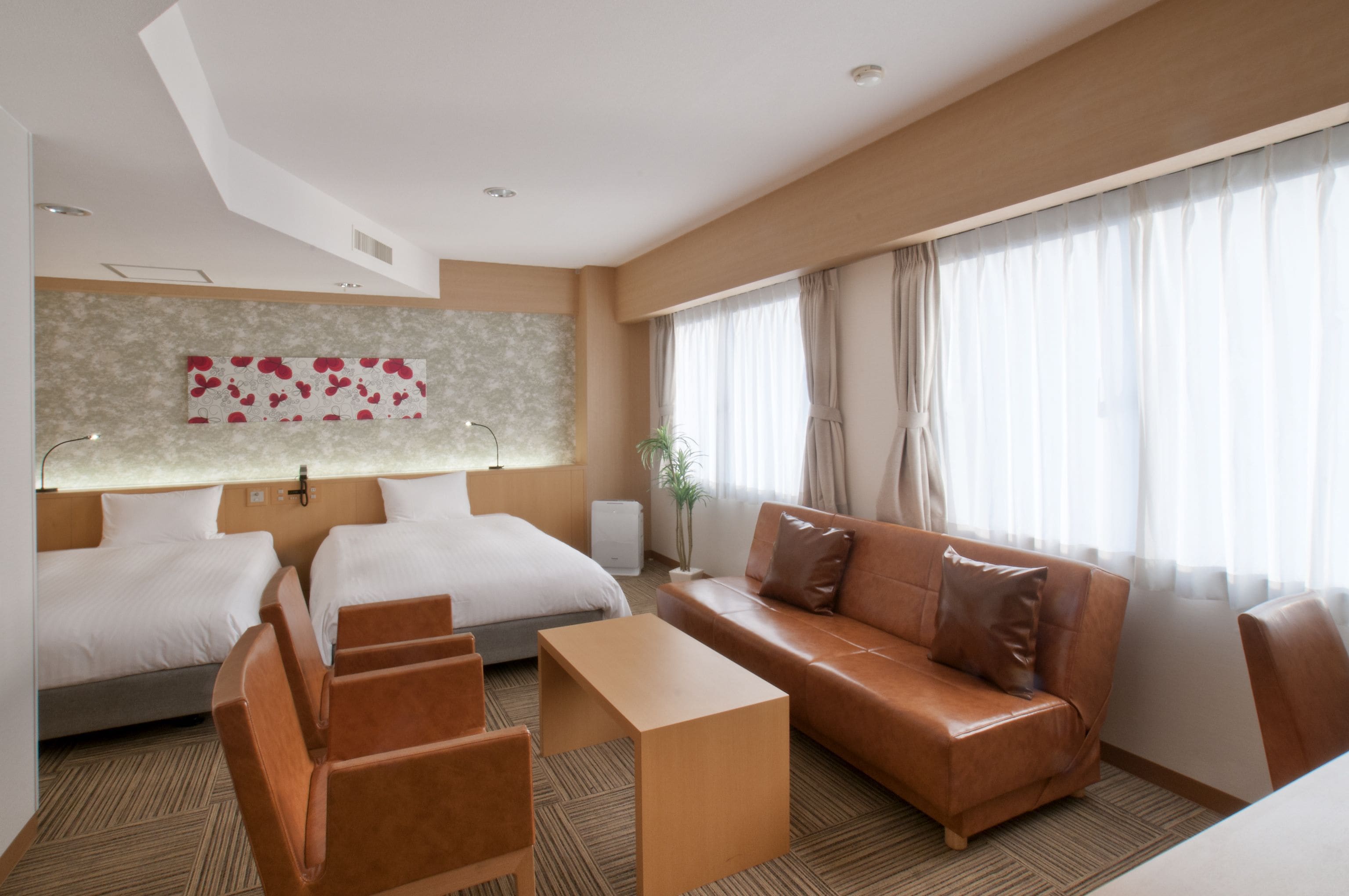 Ein Hotelzimmer mit zwei Betten, einem Sofa, einem Couchtisch und einem großen Fenster mit Vorhängen.