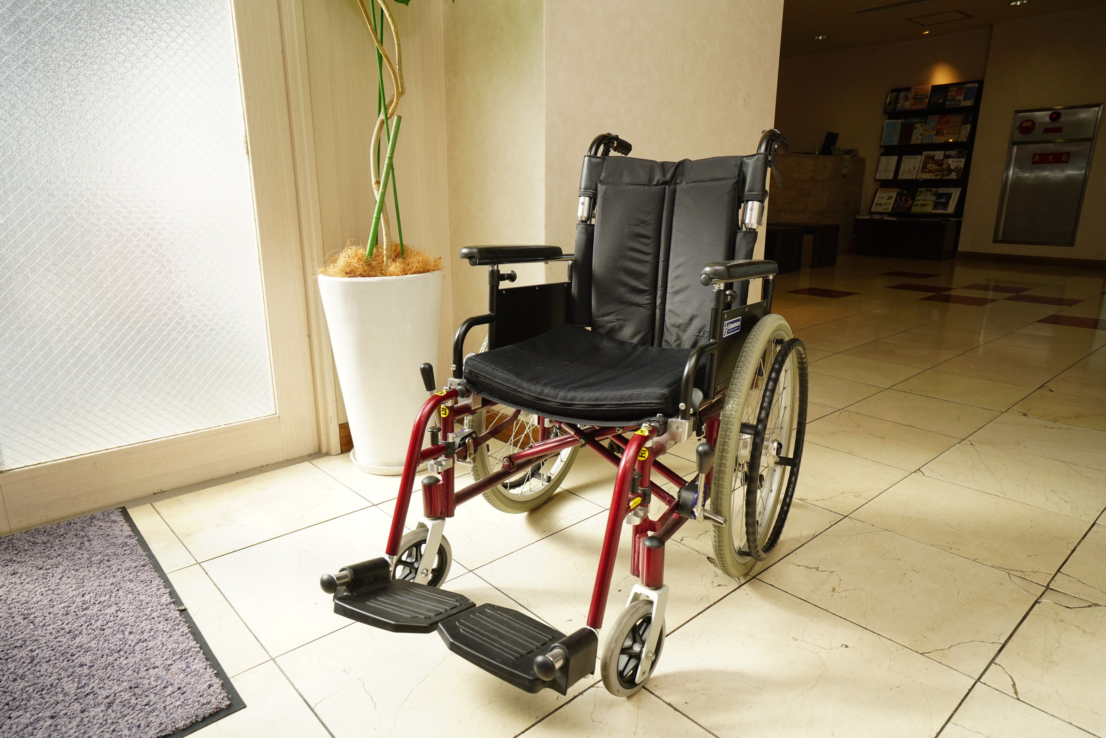 A wheelchair in a hotel lobby with a potted plant and a refrigerator in the background.