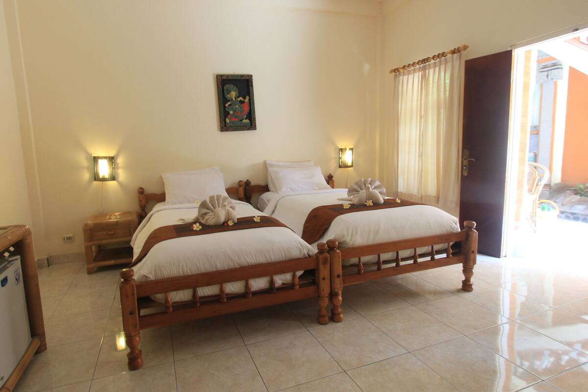 A hotel room with two wooden beds, a small desk, and a nightstand.