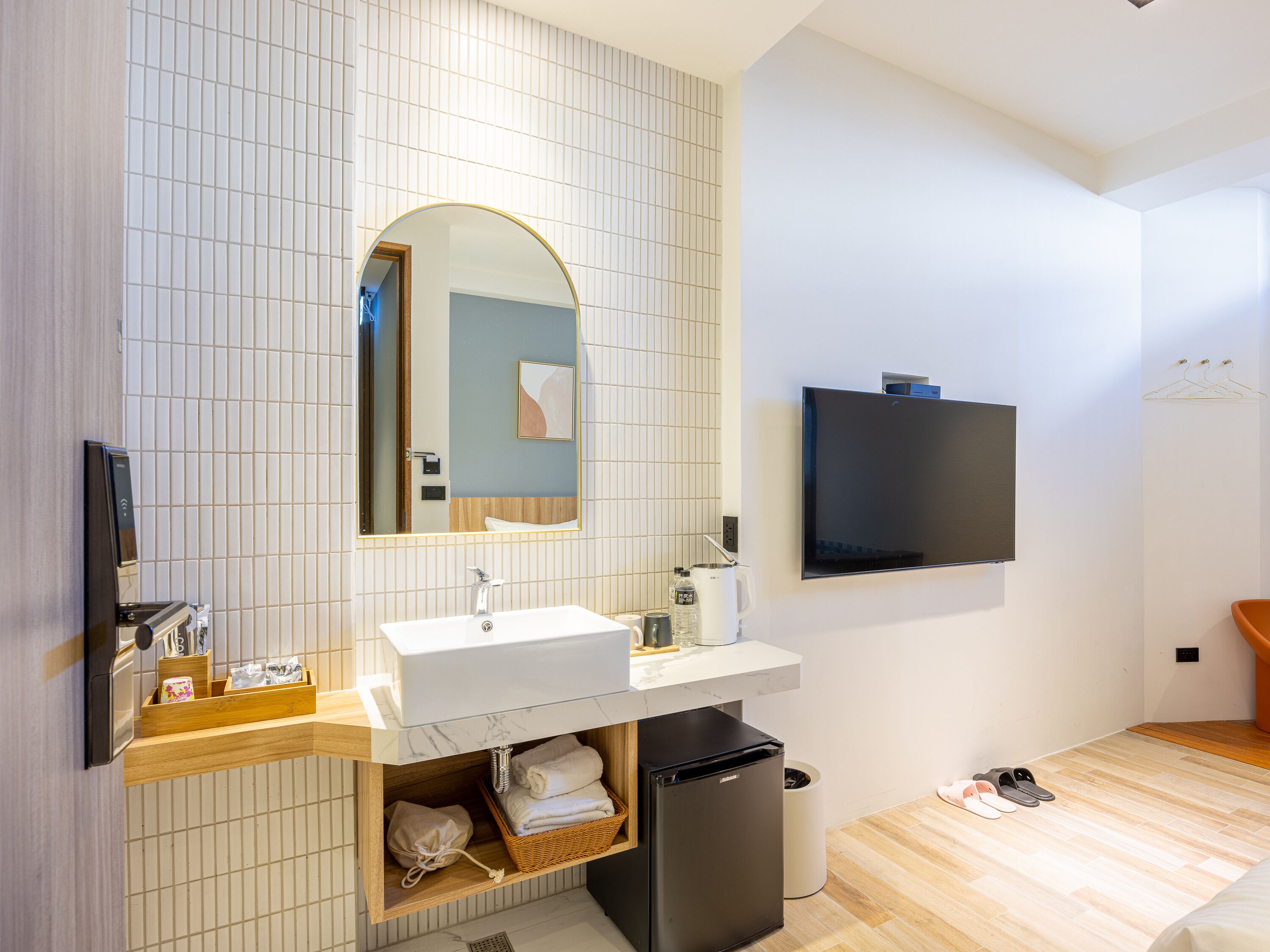 Un baño moderno con lavamanos, espejo y un refrigerador pequeño.