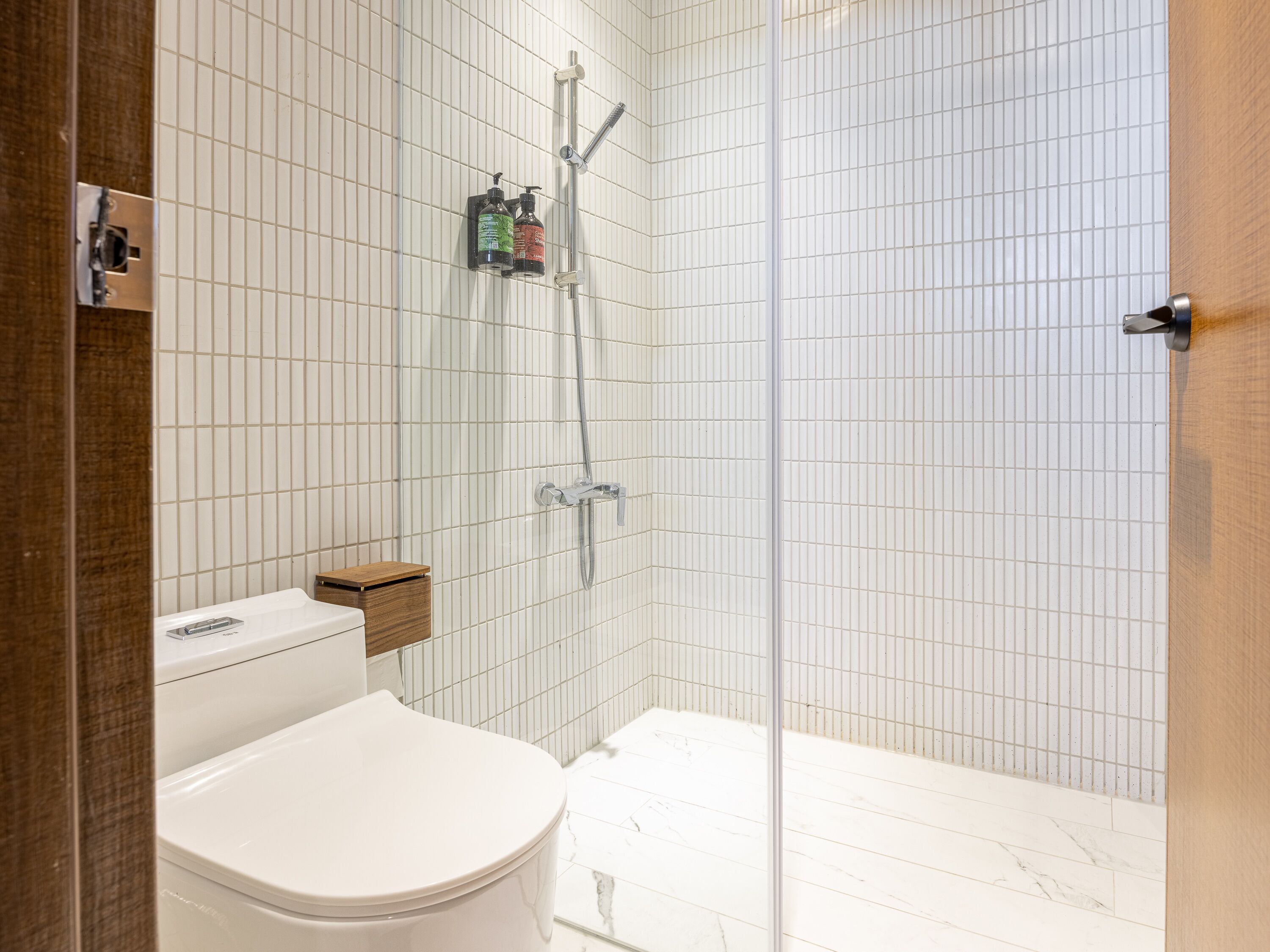 Een moderne badkamer met toilet, douche en een glazen douchecabine met handdouche.