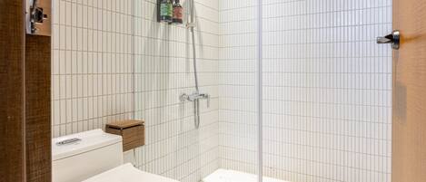 Een moderne badkamer met toilet, douche en een glazen douchecabine met handdouche.