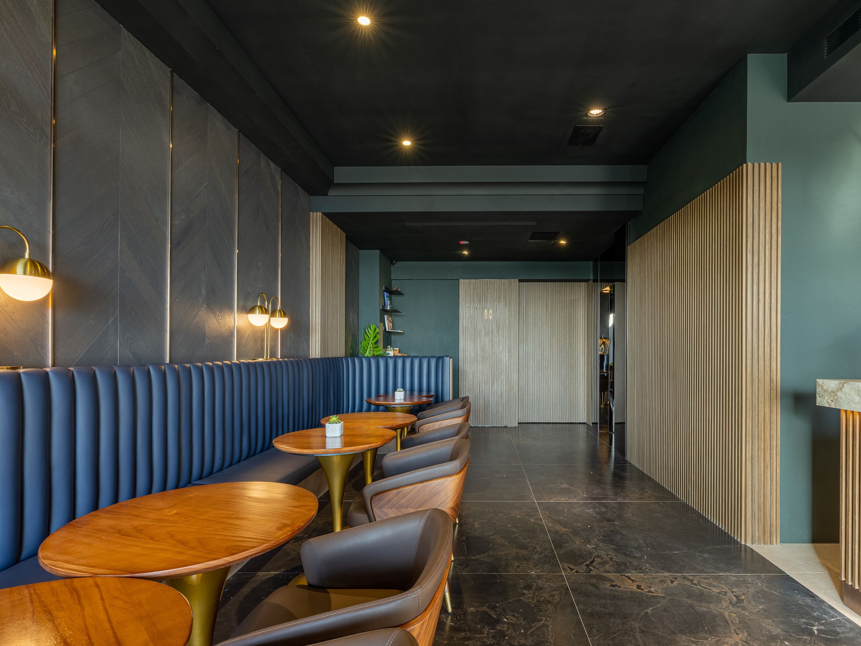A modern restaurant interior with a long counter, blue upholstered booths, and round wooden tables.