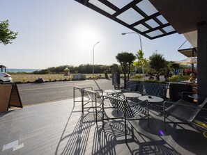 An outdoor seating area with tables and chairs, a view of the sea, and a clear sky.
