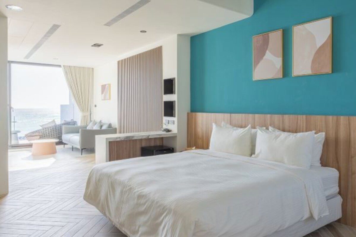 A modern hotel room with a large bed, a view of the city, and a teal accent wall.