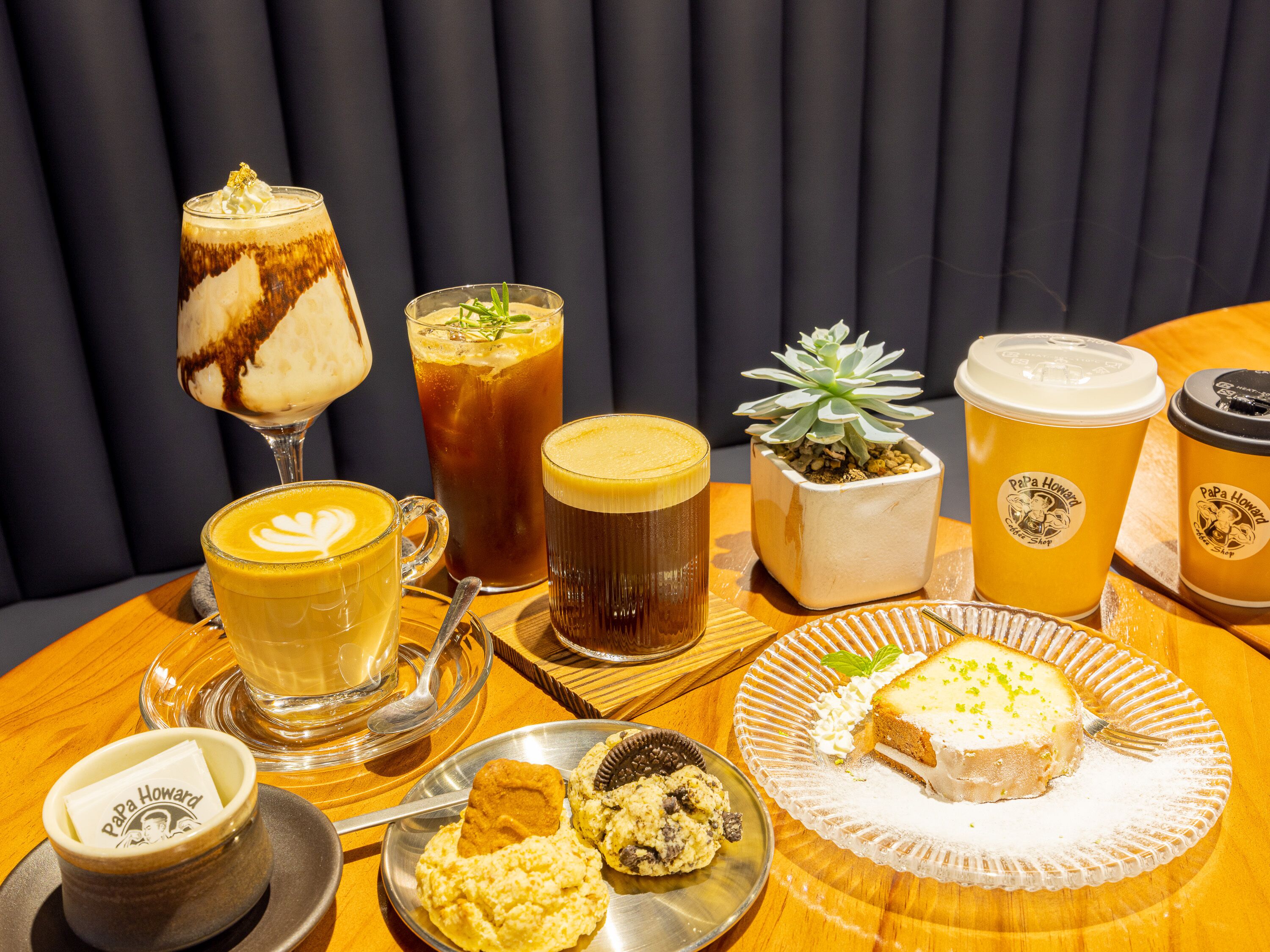 A variety of beverages and desserts on a wooden table with a potted succulent.
