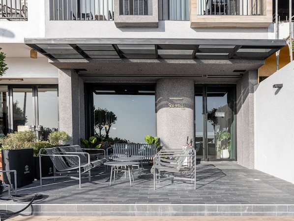 A modern building with a covered outdoor seating area, a stone pillar with "Sea wall" engraved, and a sign indicating a room number.