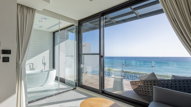 Ein modernes Badezimmer mit einer Duschkabine, einer Badewanne und einem großen Fenster mit Meerblick.