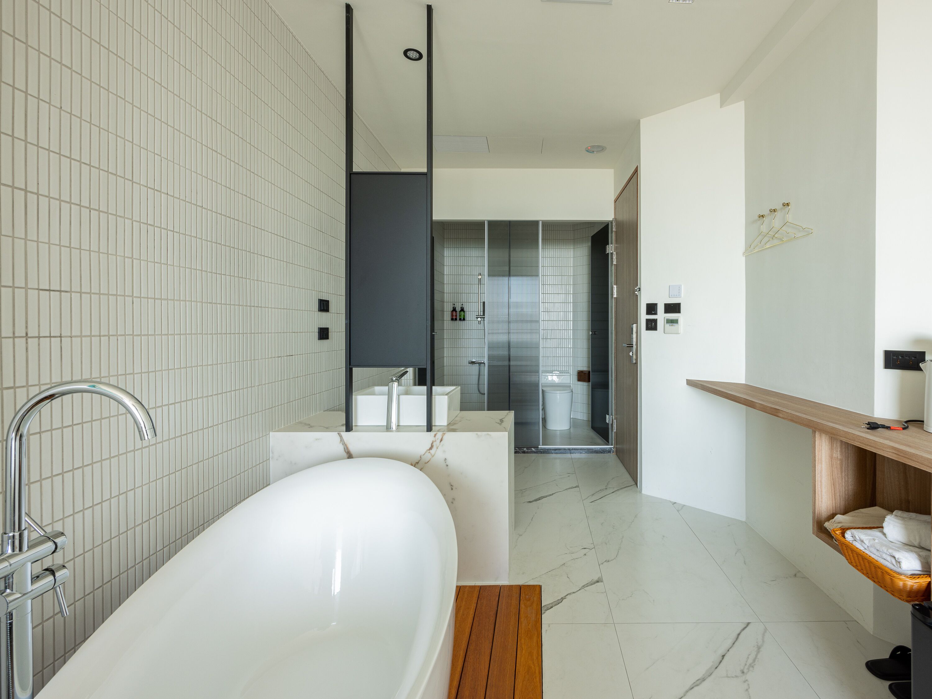 Un baño moderno con una bañera independiente, un banco de madera y una repisa de madera con toallas.