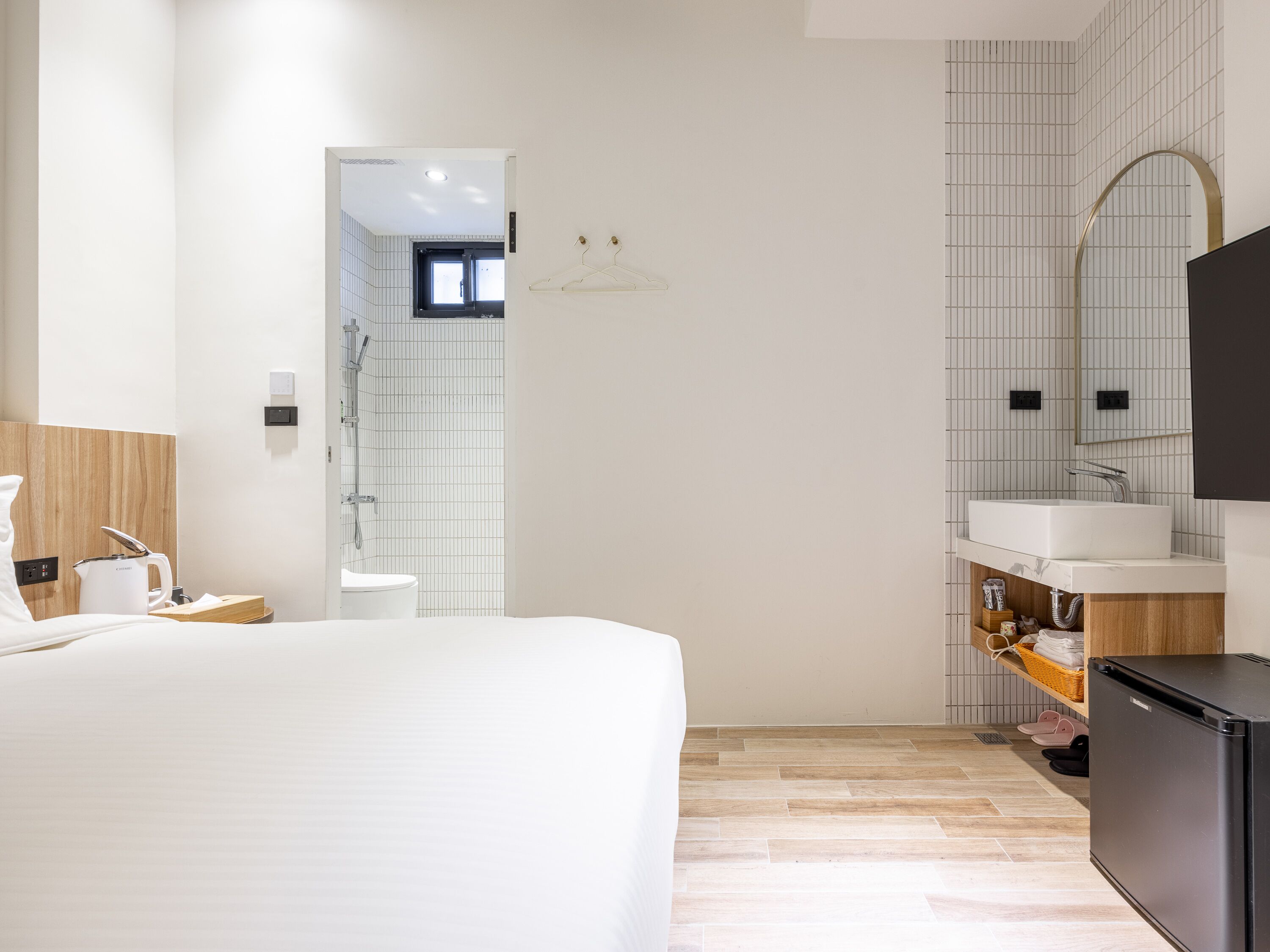 Ein modernes Hotelzimmer mit Bett, einem Badezimmer mit Dusche, Waschbecken und Fernseher.