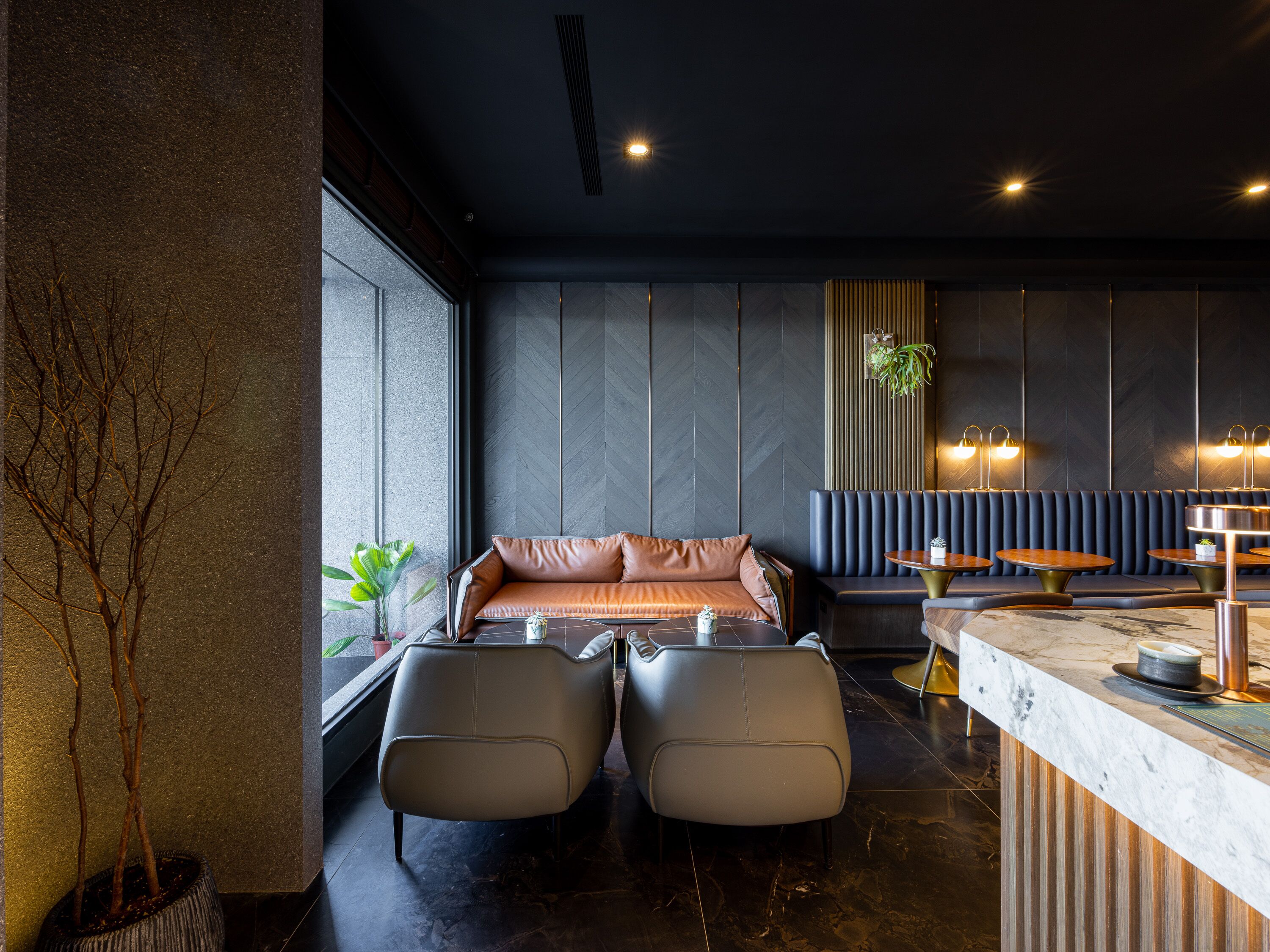 Un interior moderno con un sofá, dos sillones, una zona de bar y una planta en maceta.