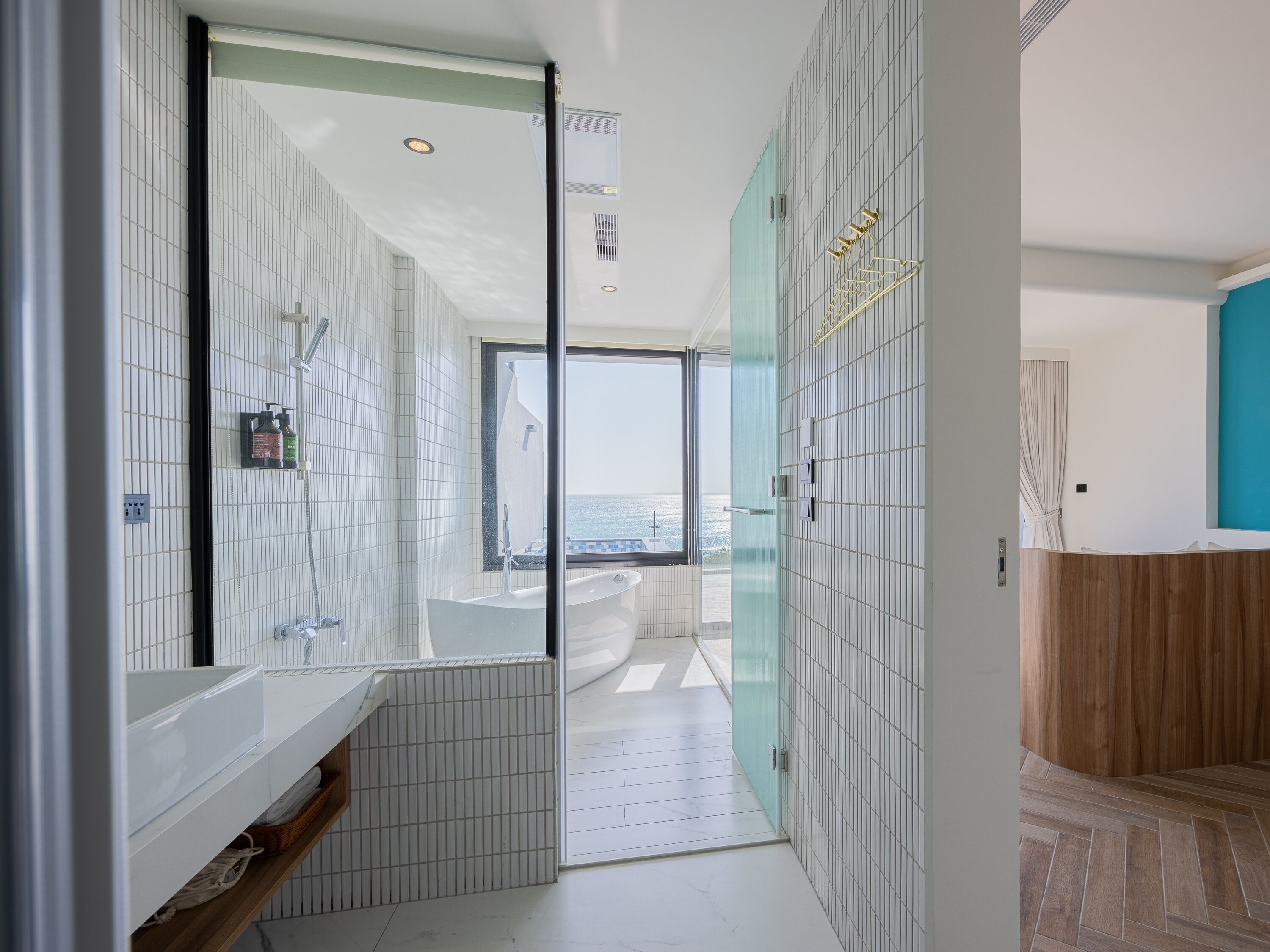 A modern bathroom with a large window, a bathtub, and a vanity with a mirror.
