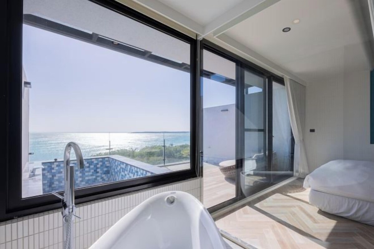 A modern bathroom with a large window, a bathtub, and a view of the sea.