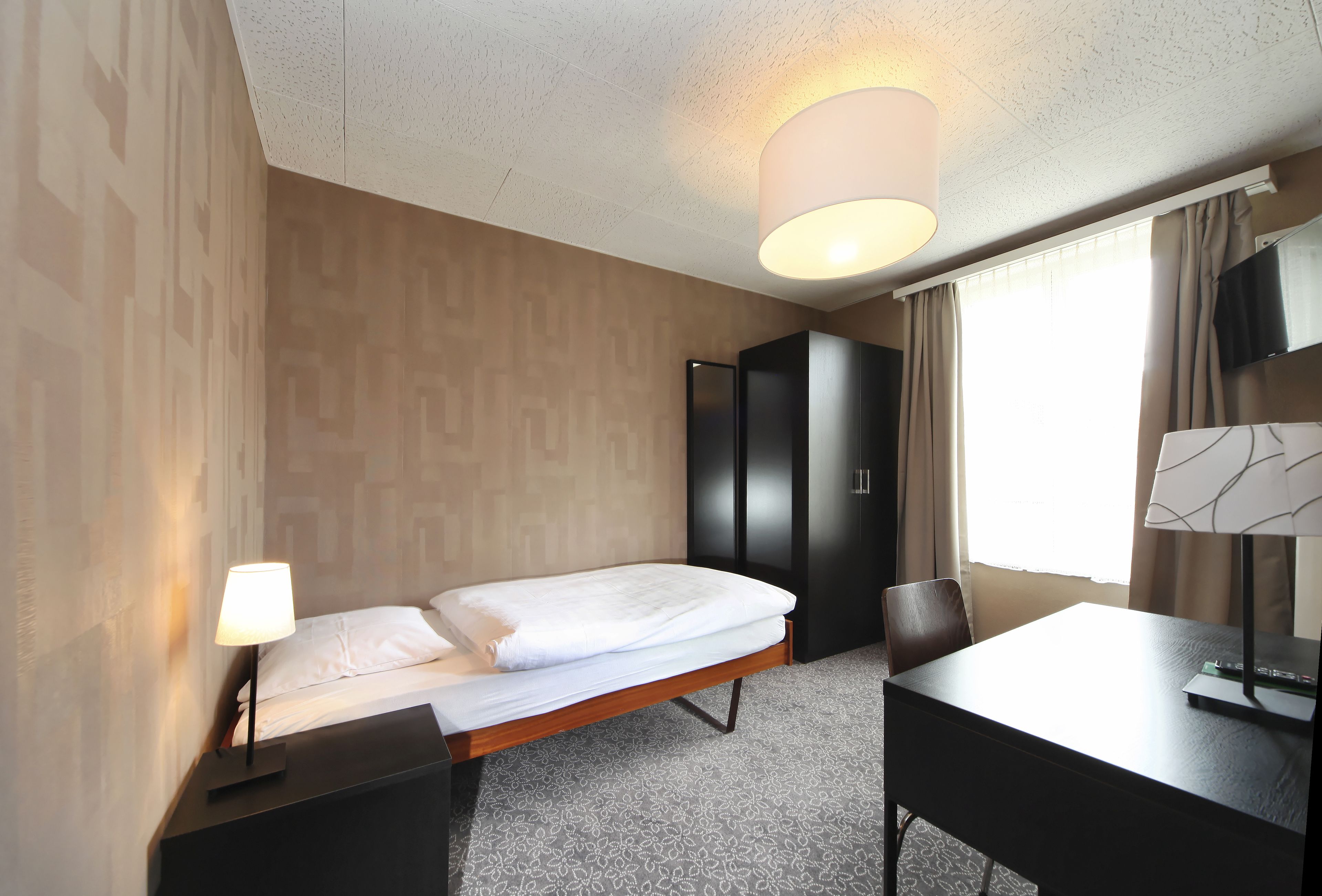 A hotel room with a bed, a desk, a chair, a wardrobe, and a television.