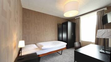 A hotel room with a bed, a desk, a chair, a wardrobe, and a television.