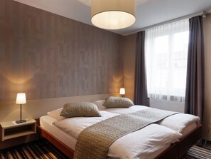 Relax in a serene space with a large bed, nightstand, and lamp, surrounded by a textured wallpaper and sheer curtains.