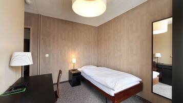 A hotel room with a bed, bedside table, lamp, desk, chair, and a large mirror.