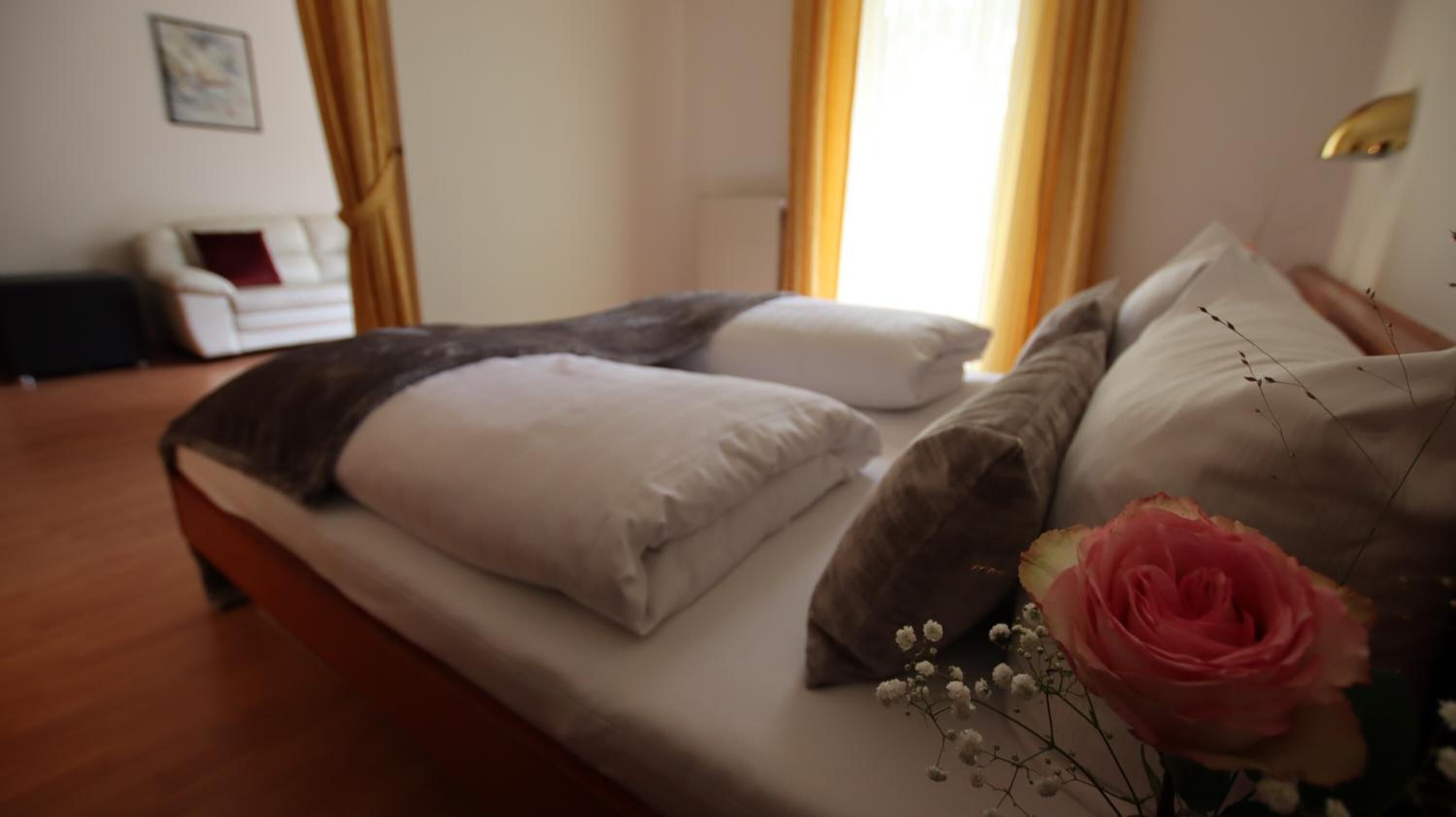 A bed with white and gray bedding, a pink rose, and white flowers.