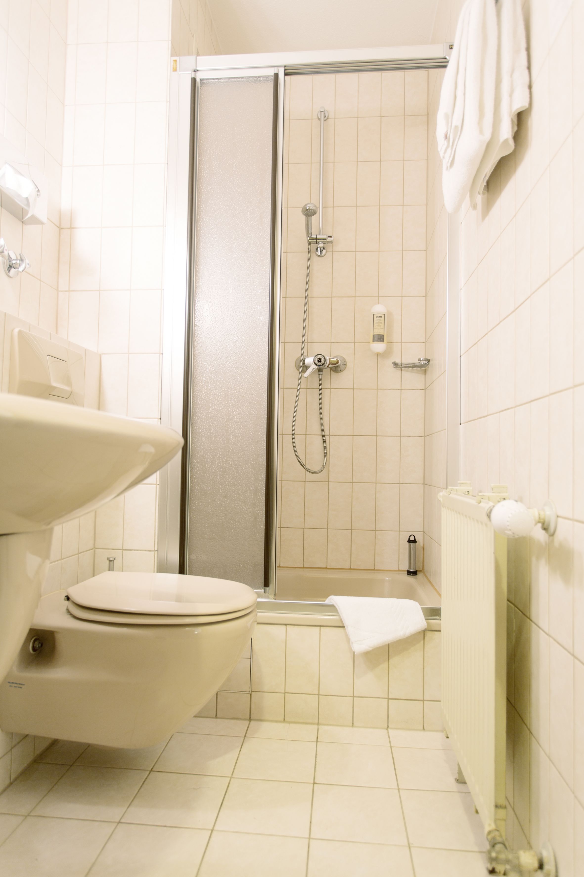 A bathroom with a toilet, sink, shower, and towel rack.