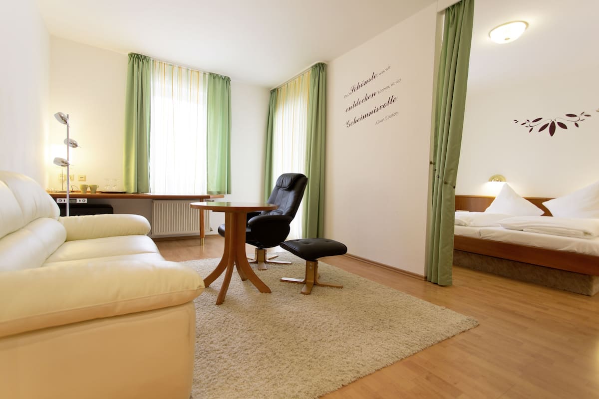 A hotel room with a bed, a sofa, a chair, a small table, and a radiator.
