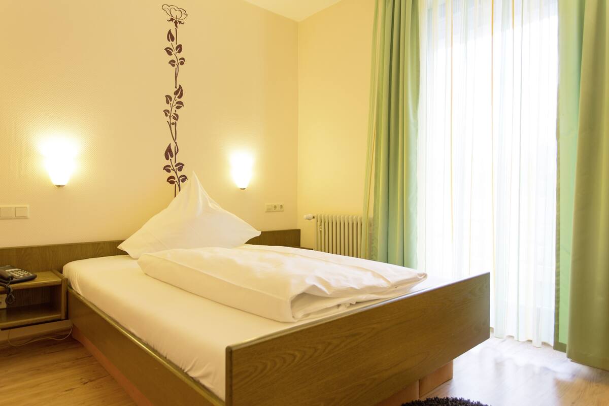 A hotel room with a wooden bed, a nightstand with a phone, and a wall-mounted light fixture.