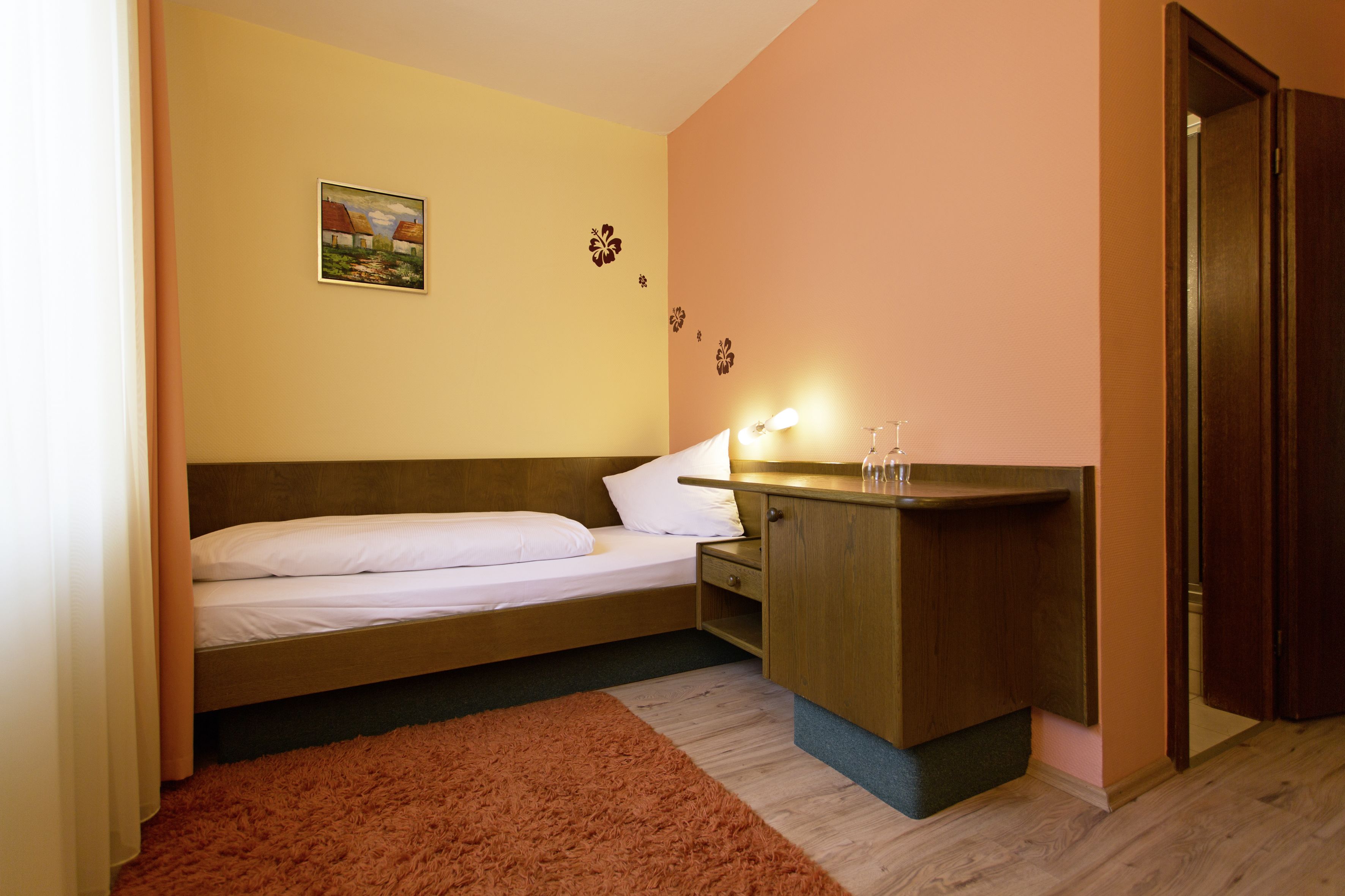A small bedroom with a bed, a wooden nightstand, a small table, and a painting on the wall.