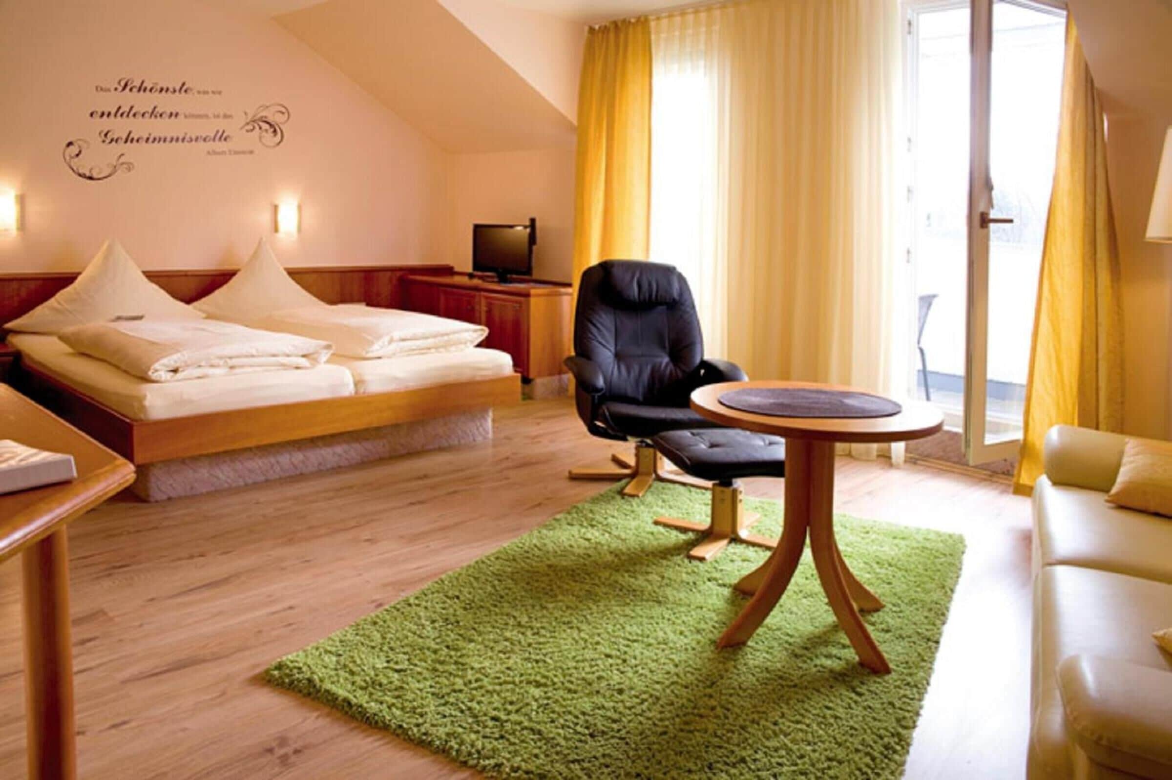 Et hotelværelse med seng, stol, lille bord og fjernsyn.