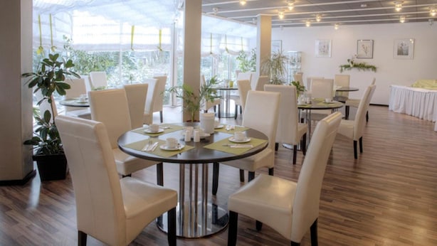 A modern dining area with round tables, white chairs, and potted plants. - Hotel Kurparkblick (Bad Bergzabern)