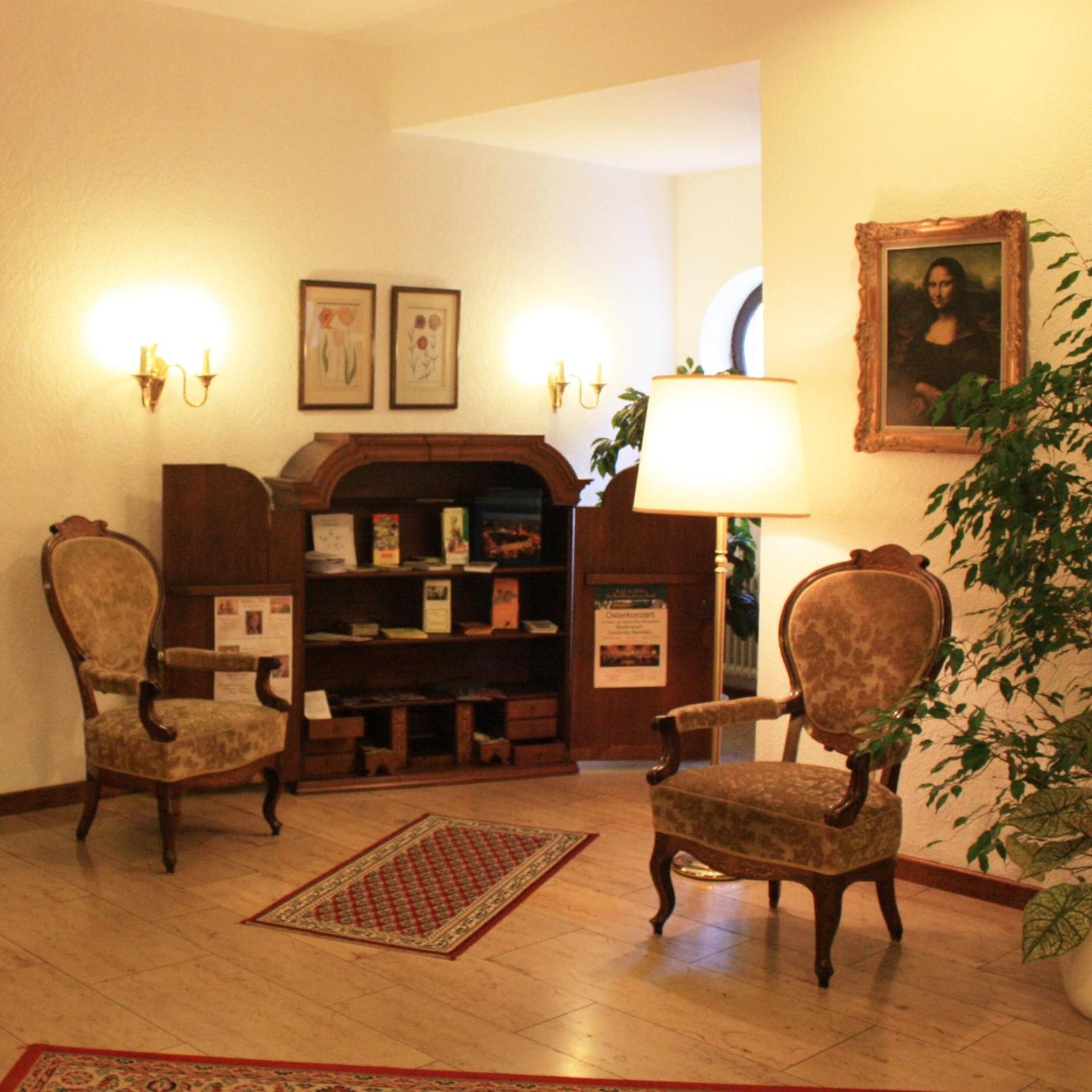 A room with two upholstered chairs, a bookshelf, a framed painting, and a lamp.