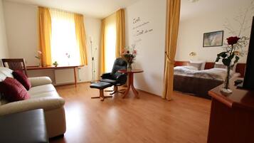 Habitación de hotel con sofá, una silla, una mesita con un florero, una cama y un cuadro en la pared.