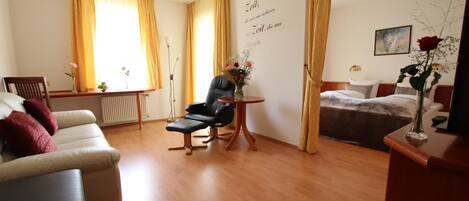 Habitación de hotel con sofá, una silla, una mesita con un florero, una cama y un cuadro en la pared.