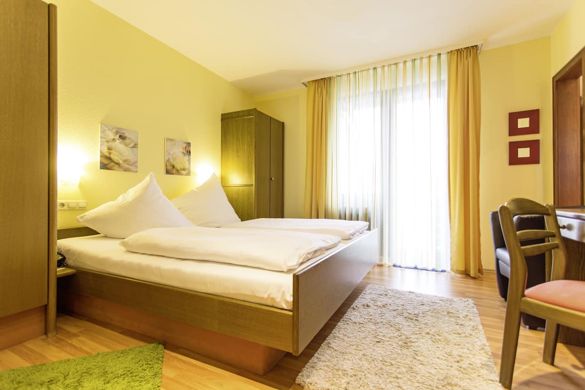 A hotel room with a double bed, a desk, a chair, a wardrobe, and two wall-mounted lights.