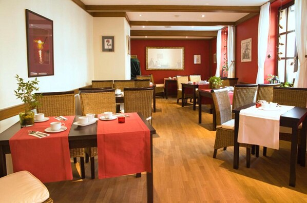 Un comedor con mesas de madera y sillas de mimbre, manteles rojos y cuadros en las paredes.