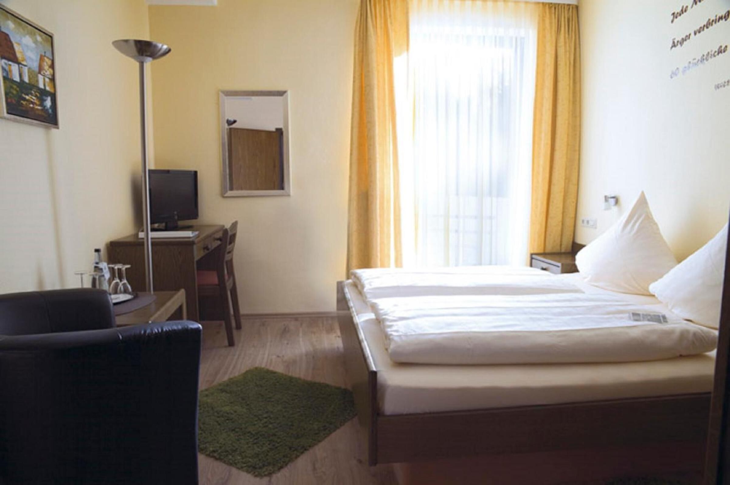 A hotel room with a bed, a desk, a chair, a TV, and a window with curtains.