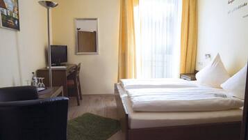A hotel room with a bed, a desk, a chair, a TV, and a window with curtains.